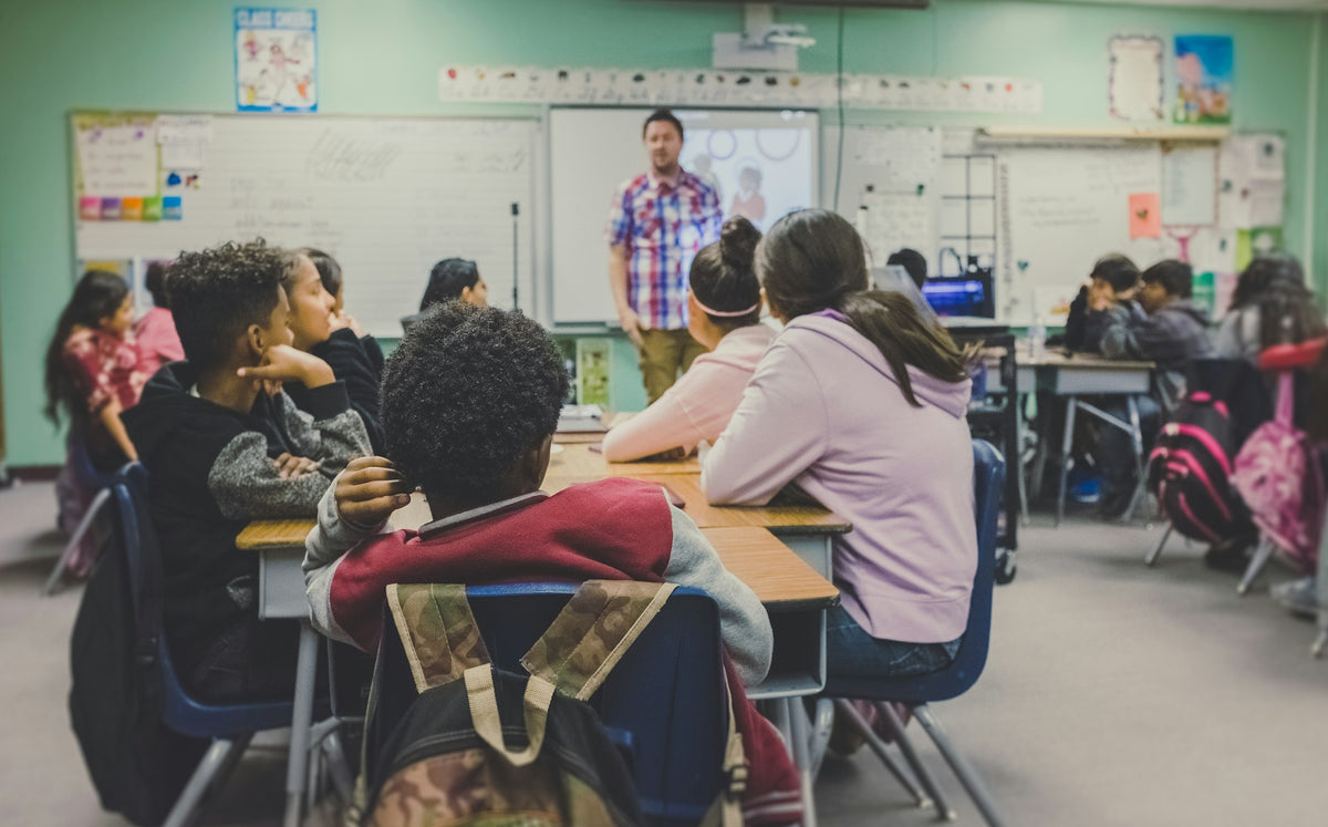 Students in a classroom facing a teacher and screen